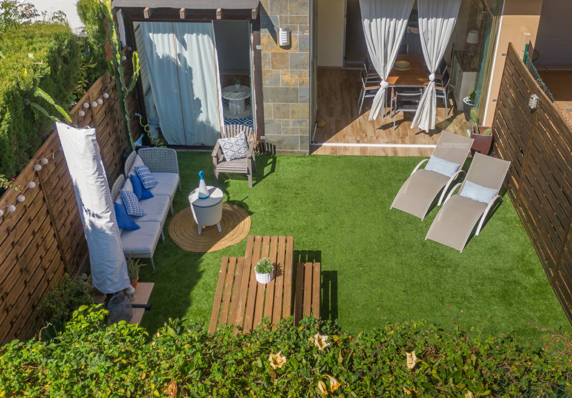 Vista aérea del jardín privado con césped, sofás exteriores y zona chill-out junto a la fachada del apartamento.