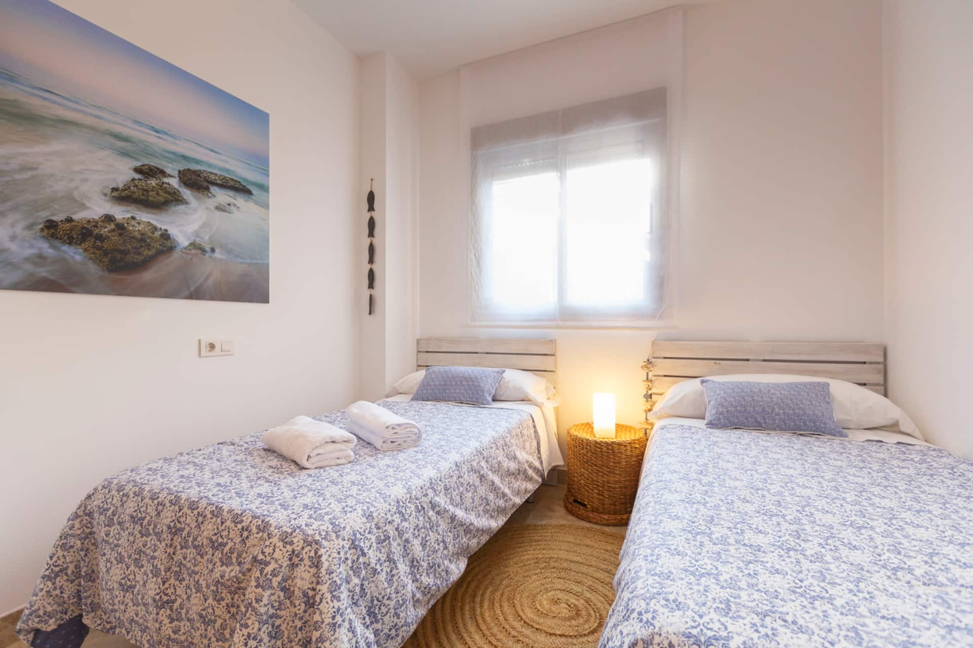 Dormitorio con dos camas individuales y una lámina de playa sobre el cabecero.