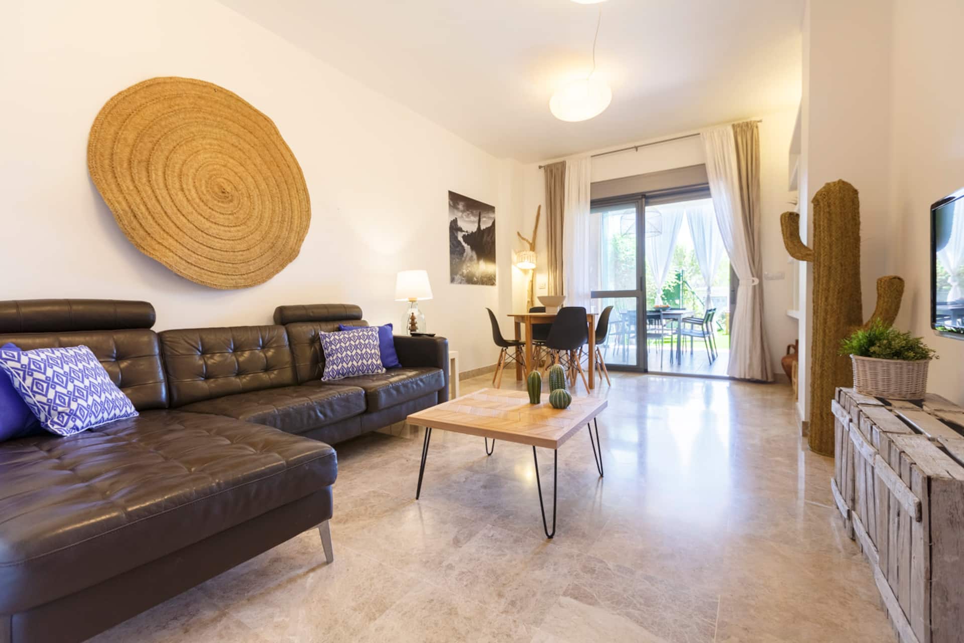Salón con sofá en piel, mesa de centro y puerta acristalada abierta al comedor exterior.