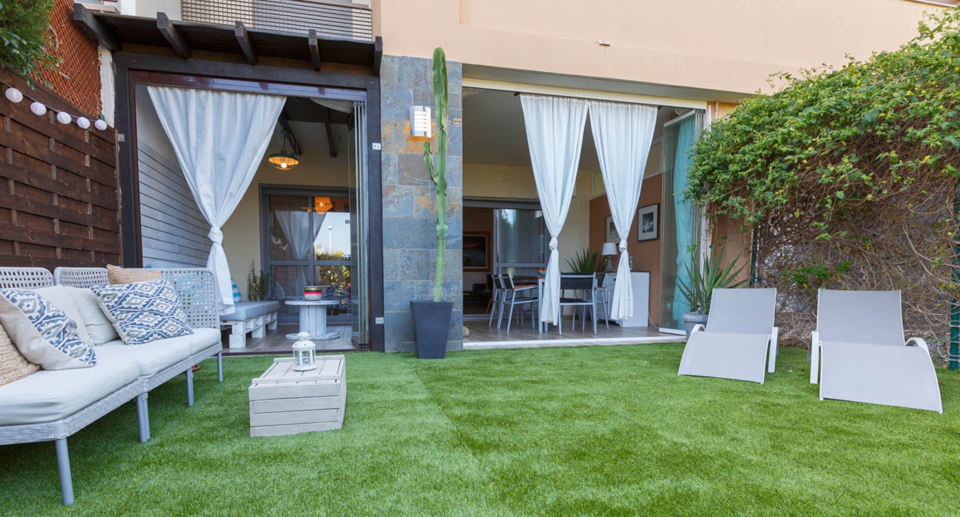 Terraza cubierta con cortinas blancas que conecta el salón interior con el jardín.