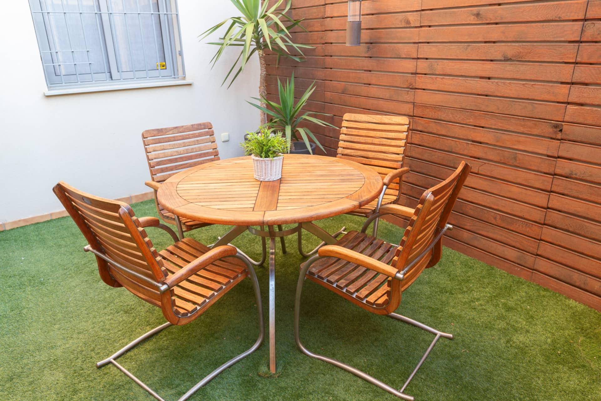 Patio con mesa redonda de madera y sillas, junto a una pared de listones.