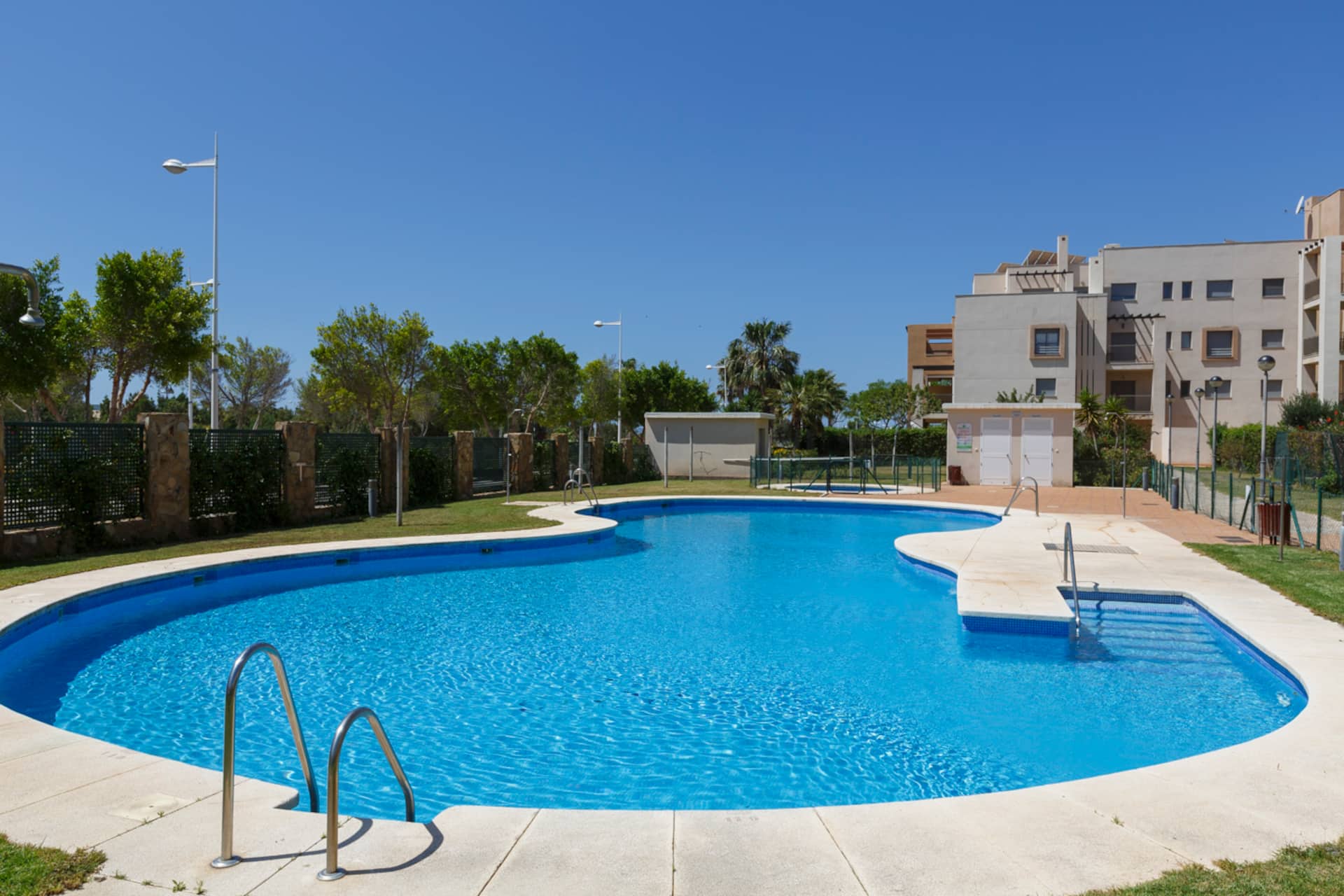Piscina comunitaria exterior con césped y zona de tumbonas alrededor.