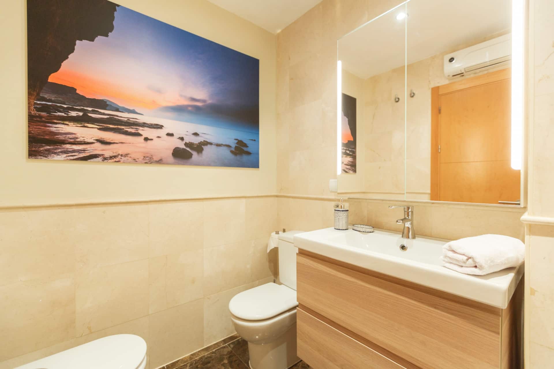 Baño completo con bañera, mueble de lavabo en madera y fotografía de playa.