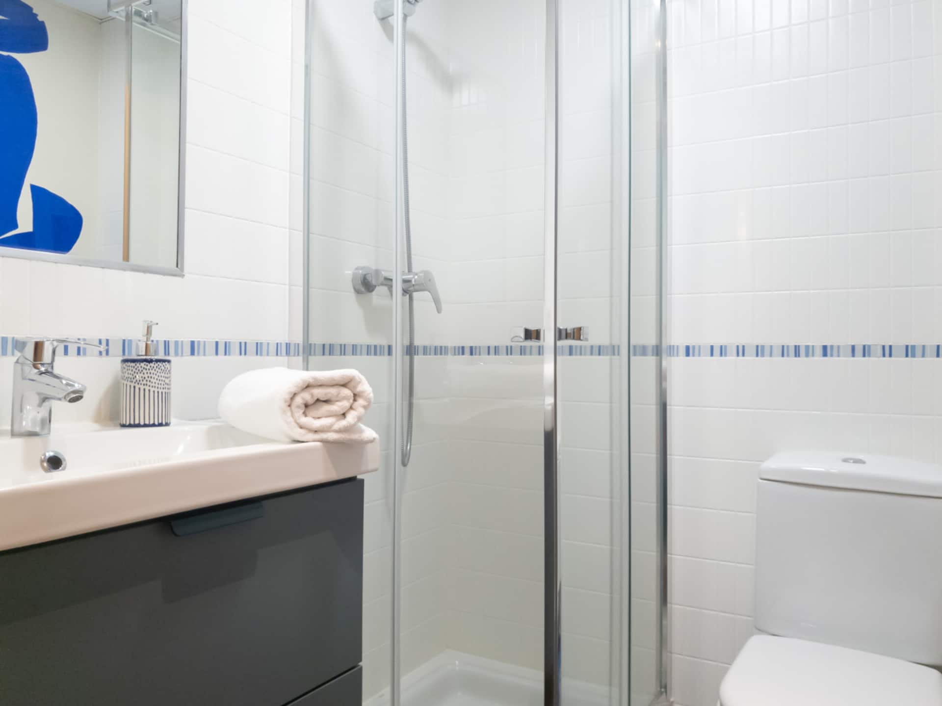 Baño con ducha de obra y mampara de cristal, en tonos azules.
