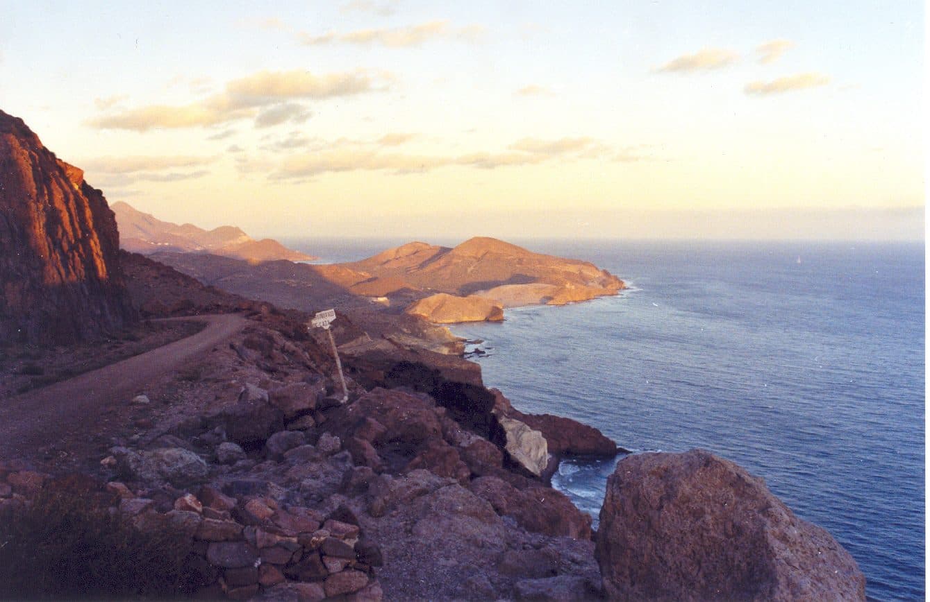 Sendero costero del Cabo de Gata al atardecer, con un cartel de ruta junto al acantilado.