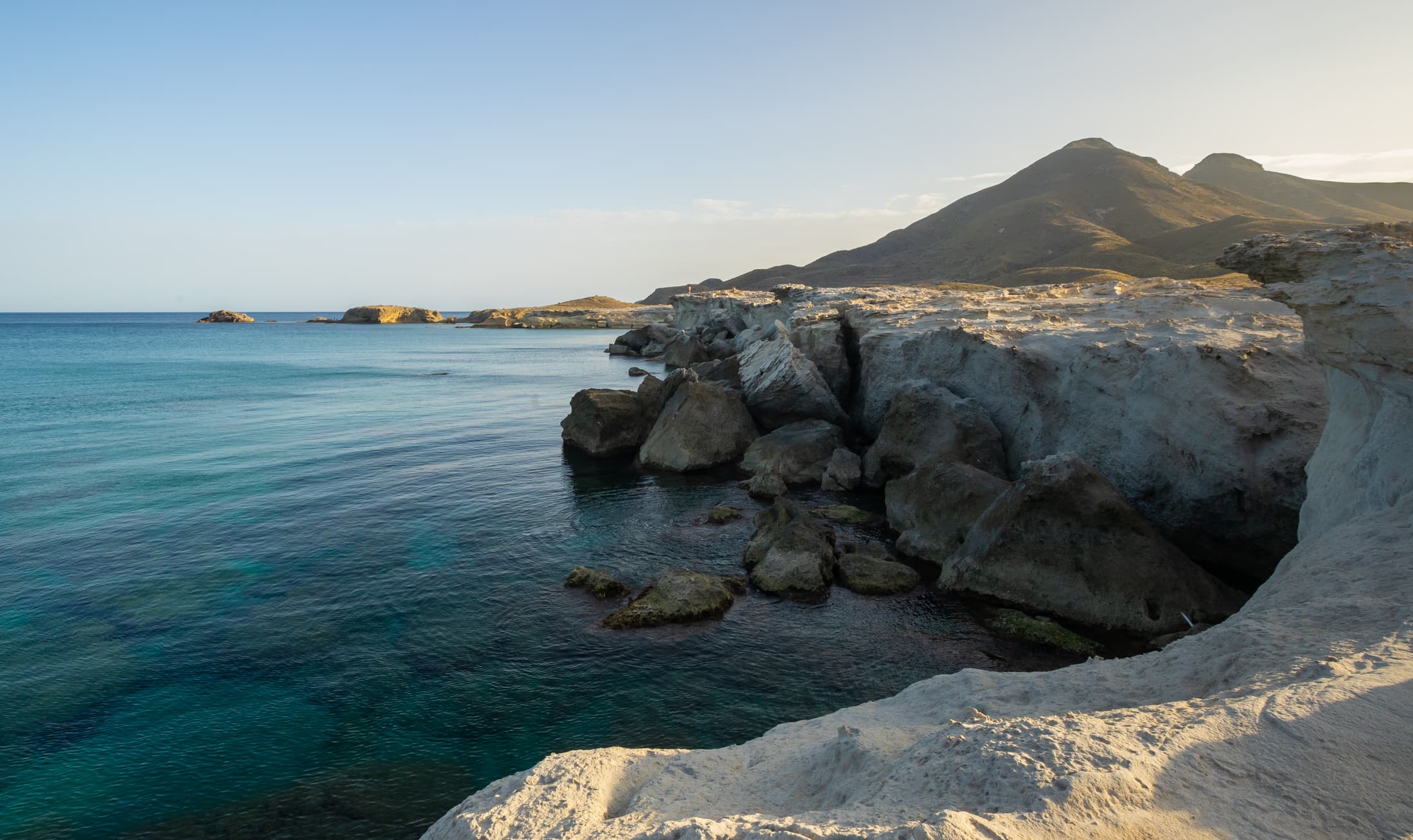 Cala de agua transparente entre roca clara y montañas de Cabo de Gata.